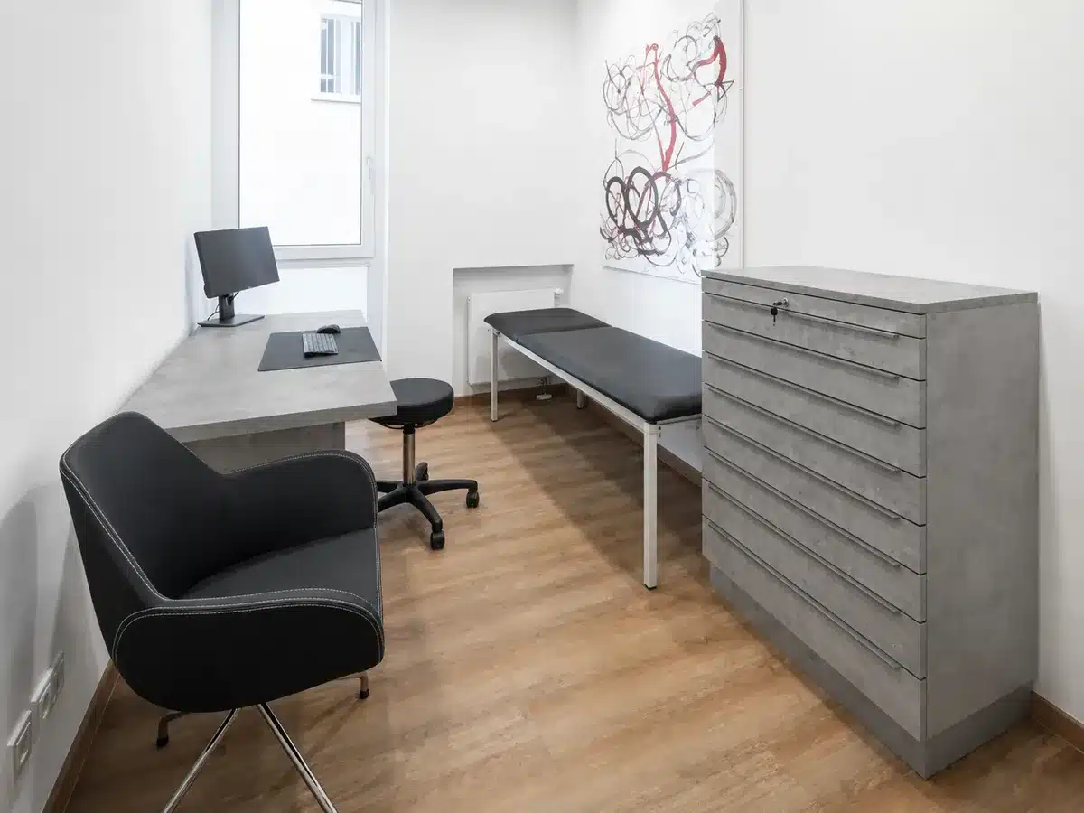 Arzt-Behandlungszimmer mit erneuerten Schrank- und Tischoberflächen in Betonoptik und hellem Eichenboden.